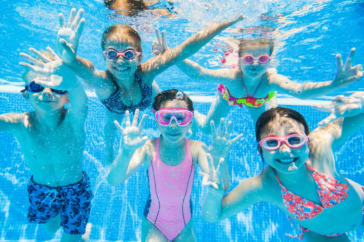Children swimming underwater wearing colorful goggles and waving happily